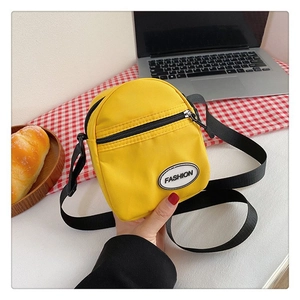 Detalle de bolso bandolera de nailon amarillo con bolsillo frontal y parche de moda