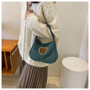Close-up of a green fabric handbag featuring a cute brown plush bear embroidery
