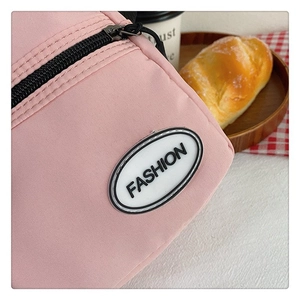 Detalle de un bolso de lona rosa con cremallera negra y etiqueta de moda