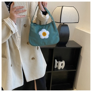 Close-up of green nylon handbag featuring white flower and yellow smiley face embroidery