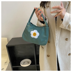 Detail of dark green nylon baguette bag featuring a large white flower smile patch