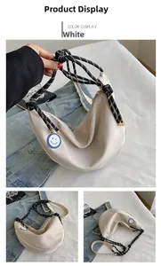Détail du sac croissant en toile blanche avec anse tressée et patch smiley bleu