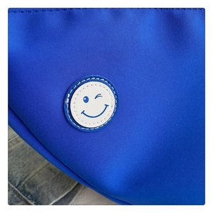 Vue détaillée d'un sac en toile bleu avec un écusson brodé blanc d'un visage souriant