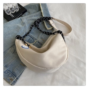 Détail du sac beige en demi-lune avec patch smiley bleu et bandoulière tissée