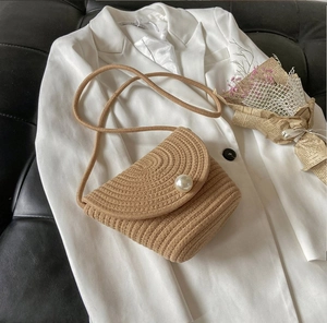 Detail of hand-woven beige straw crossbody bucket bag with pearl accent and fine rope strap
