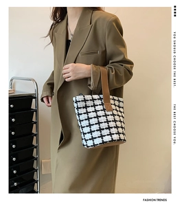 Close-up of black and white plaid woven tote bag with brown leather shoulder strap