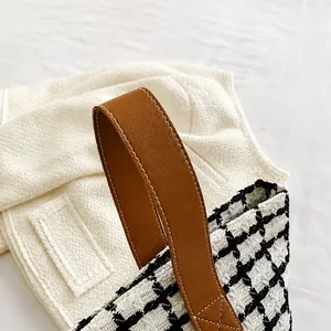 Detail of leather handles with stitching on a black and white plaid tweed tote bag