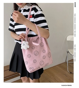 Detailed close-up of a pink corduroy tote bag featuring black smile patterns and a plush charm