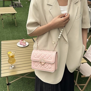 Pink quilted shoulder bag with pearl chain strap and gold buckle in an outdoor setting