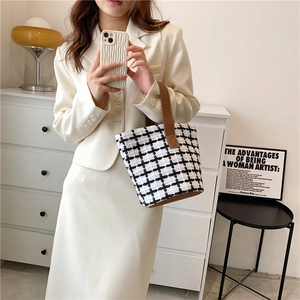 Chic black and white tweed plaid bucket bag with brown leather handles held by a model