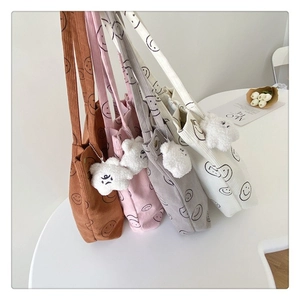 Detail of soft corduroy tote bags with smiley print and plush doll charm in four colors
