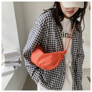 Detalle del bolso de media luna en nailon naranja con correa ajustable en una modelo