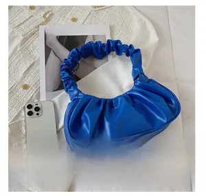 Detail view of the blue pleated cloud bag showing fabric texture with a phone for size reference