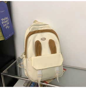 Detail showing plush bunny ears design and fashion logo on cream canvas backpack