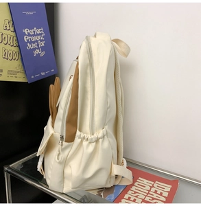 Side view of beige nylon backpack featuring elastic water bottle pocket and rabbit ear detail