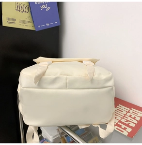 Detail view of the cream-colored canvas backpack with a buckle flap and thick woven strap