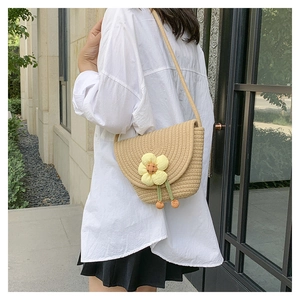 Detalle de bolso tipo cubo de paja tejida con una flor de margarita amarilla beige