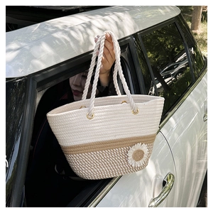 Close-up of woven tote bag with 3D daisy flowers and thick rope handles in a car