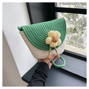 Detalle de bolso saco tejido con solapa verde, cuerpo crema y dije de flor amarilla