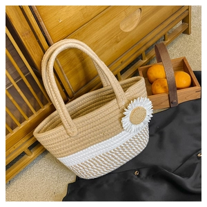 Detailed shot of straw tote bag with white daisy flower charm and woven handle