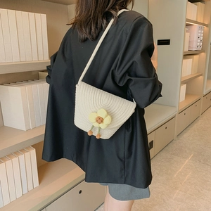 Bolso tipo cubo tejido crema con dije de flor amarilla usado por modelo en entorno minimalista
