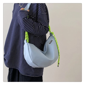Detail of light blue nylon crescent bag featuring a neon green braided rope shoulder strap