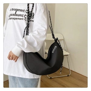 Detail of black crescent crossbody bag with thick black and white striped rope strap
