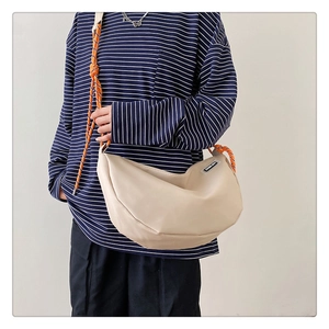 Detail of beige nylon crescent crossbody bag with orange woven rope strap and logo label
