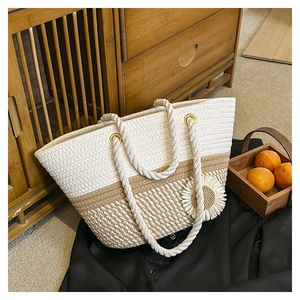Handwoven cream and oat straw tote bag with daisy floral charm in home setting