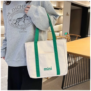 Detalle del bolso tote de lona blanca con bordado verde y asas superiores