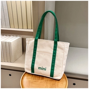 Detalle de bolsa tote de lona con asas verdes y bordado mini sobre taburete de madera