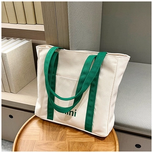 Detalle de bolso tote de lona crema con asas verdes y bolsillo frontal abierto