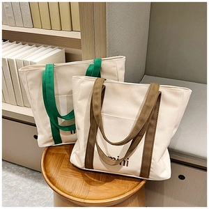 Detalle de bolsos tote de lona con estampado mini y asas de colores sobre taburete de madera