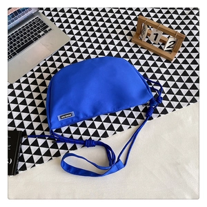 Detail of Klein blue nylon crescent bag with knot strap and branded label on desk
