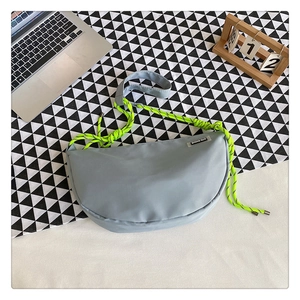 Close-up of light blue nylon crescent bag with neon green rope strap in casual setting