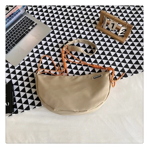 Flat lay of beige nylon crescent bag with woven rope strap and lifestyle props