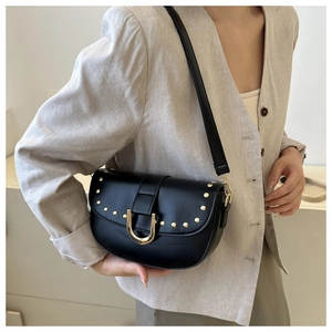 Détail d'un sac selle noir avec clous dorés et boucle en U sur un blazer en lin
