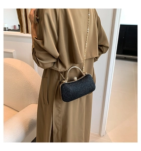 Detailed view of a black glitter evening clutch with gold metal handle and chain strap
