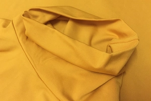 Macro detail of mustard yellow knit fabric with ribbed texture and turtleneck stitching