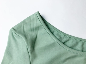 Detailed close-up of light green knit fabric neckline featuring fine double-needle stitching