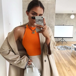 Gros plan d'un body dos nu orange vif porté avec un trench beige et une chaîne en métal