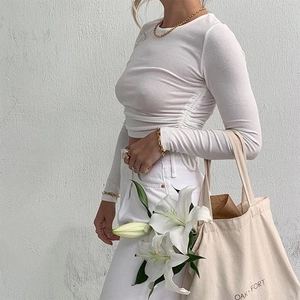 Detail of white ribbed long sleeve crop top with side drawstring ruching and slim fit design