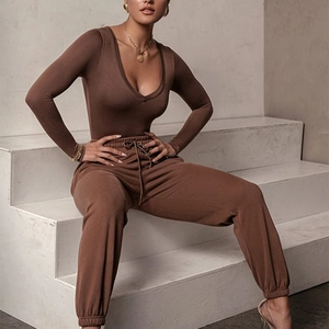 Close-up of deep V-neck brown bodysuit and matching joggers on sitting model
