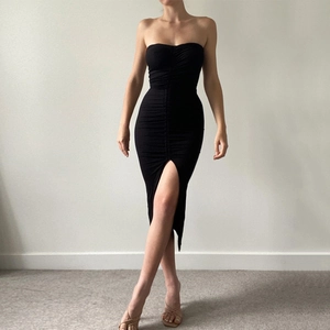 Detail view of ruched fabric and side slit on this sexy black strapless slim-fit dress