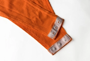 Détail du bas de body orange côtelé avec trois boutons-pression pour la fermeture