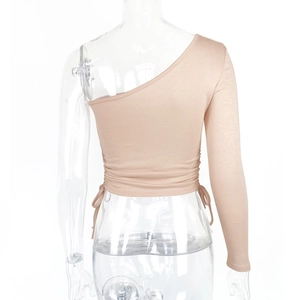 Detail of skin-toned one-shoulder long sleeve crop top with side drawstring ruching