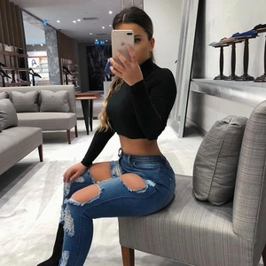 Detail of high-waisted distressed jeans with ripped knees and fitted black crop top