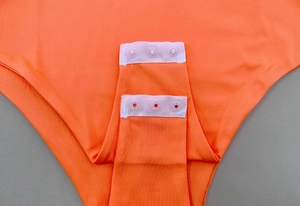 Detail view of the bright orange bodysuit showing secure triple snap button closure at the crotch
