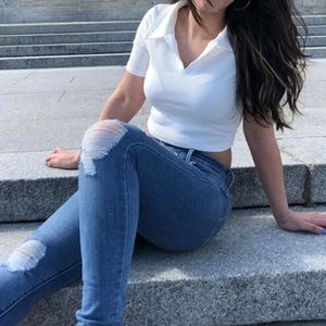 Détail d'un haut polo blanc court avec un jean en denim bleu moulant et déchiré