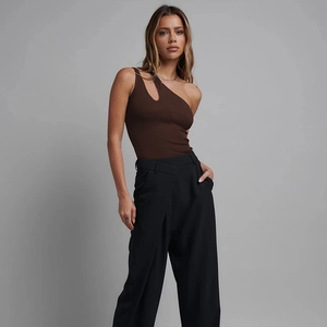 Detail eines dunkelbraunen One-Shoulder-Bodys aus Rippbaumwolle mit schwarzer weiter Hose